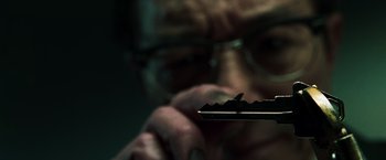Movie still from “The Matrix Reloaded” (2003), directed by Lana Wachowski – A man in glasses looking down at a piece of metal; Extreme Close Up shot, High angle