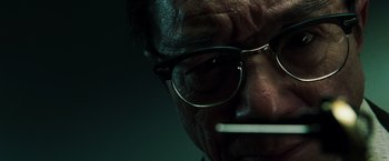 Movie still from “The Matrix Reloaded” (2003), directed by Lana Wachowski – An older man wearing glasses and smoking a cigarette; Extreme Close Up shot, Low angle