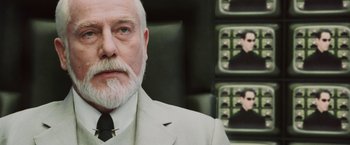 Movie still from “The Matrix Reloaded” (2003), directed by Lana Wachowski – An older man in a suit and a tie; Close Up shot, Over the shoulder angle