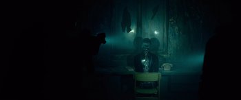 Movie still from “The Matrix Resurrections” (2021), directed by Lana Wachowski – A man sitting at a table in front of a projector; Wide shot, Over the shoulder angle