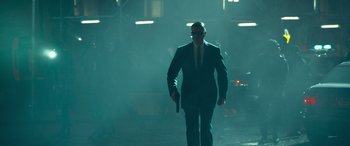 Movie still from “The Matrix Resurrections” (2021), directed by Lana Wachowski – A man in a suit and tie holding a gun; Wide shot, Low angle
