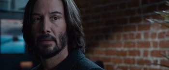 Movie still from “The Matrix Resurrections” (2021), directed by Lana Wachowski – A person with long hair and a beard; Close Up shot, Over the shoulder angle