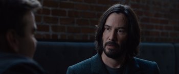 Movie still from “The Matrix Resurrections” (2021), directed by Lana Wachowski – A man with long hair and a beard sitting on a couch; Close Up shot, Over the shoulder angle