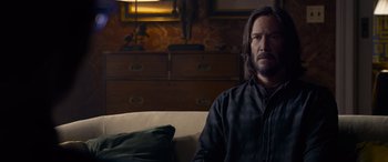 Movie still from “The Matrix Resurrections” (2021), directed by Lana Wachowski – A man sitting on top of a couch in a living room; Medium shot, Over the shoulder angle