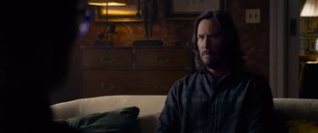 Movie still from “The Matrix Resurrections” (2021), directed by Lana Wachowski – A man sitting on top of a couch in a living room; Medium shot, Over the shoulder angle