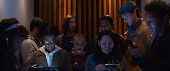 Movie still from “The Matrix Resurrections” (2021), directed by Lana Wachowski – A group of people standing around each other looking at cell phones; Medium shot, Low angle
