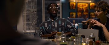 Movie still from “The Matrix Resurrections” (2021), directed by Lana Wachowski – A man sitting at a table with a glass in front of him; Medium shot, Over the shoulder angle