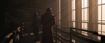 Movie still from “The Matrix Resurrections” (2021), directed by Lana Wachowski – A man in a red coat is standing next to a window; Wide shot, Over the shoulder angle