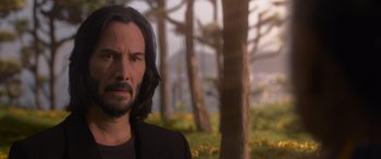 Movie still from “The Matrix Resurrections” (2021), directed by Lana Wachowski – A man with long black hair standing in front of trees; Close Up shot, Over the shoulder angle