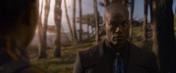 Movie still from “The Matrix Resurrections” (2021), directed by Lana Wachowski – A man in a suit and tie standing in front of trees; Medium shot, Low angle
