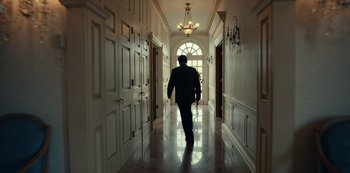 Movie still from “Dopesick” (2021), directed by Danny Strong – A man walking down a hall way in a house; Wide shot, Low angle