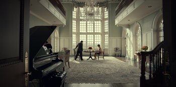 Movie still from “Dopesick” (2021), directed by Danny Strong – A man and a woman are sitting at a table in a large room; Extreme Wide shot, Low angle