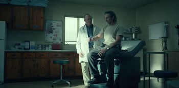 Movie still from “Dopesick” (2021), directed by Danny Strong – A man sitting in a chair in front of a doctor; Medium shot, Low angle