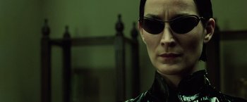Movie still from “The Matrix Revolutions” (2003), directed by Lilly Wachowski – A woman wearing sunglasses and a black leather jacket; Close Up shot, Over the shoulder angle