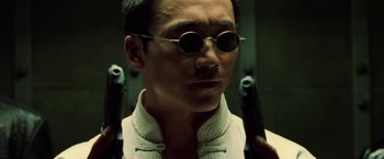 Movie still from “The Matrix Revolutions” (2003), directed by Lilly Wachowski – A man in white jacket and round sunglasses holding two guns; Close Up shot, Low angle
