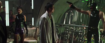 Movie still from “The Matrix Revolutions” (2003), directed by Lilly Wachowski – A man standing next to a railing holding a gun in his hand; Medium shot, Over the shoulder angle