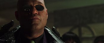 Movie still from “The Matrix Revolutions” (2003), directed by Lilly Wachowski – A man wearing sunglasses and a tie; Close Up shot, Low angle