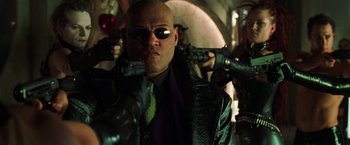 Movie still from “The Matrix Revolutions” (2003), directed by Lilly Wachowski – A man with a green tie and a green jacket holding two guns; Medium shot, Low angle