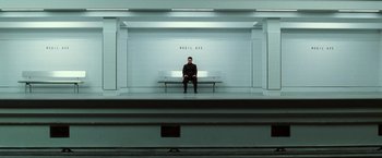 Movie still from “The Matrix Revolutions” (2003), directed by Lilly Wachowski – A man sitting on top of a bench in a room; Extreme Wide shot, High angle