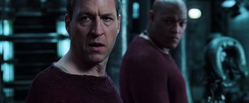 Movie still from “The Matrix Revolutions” (2003), directed by Lilly Wachowski – A man in a purple sweater standing next to another man; Close Up shot, Over the shoulder angle