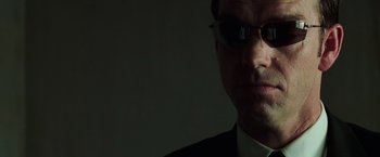 Movie still from “The Matrix Revolutions” (2003), directed by Lilly Wachowski – A person wearing a suit and sunglasses; Extreme Close Up shot, Low angle