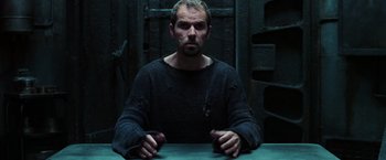 Movie still from “The Matrix Revolutions” (2003), directed by Lilly Wachowski – A man sitting at a table in a dark room; Medium shot, Low angle