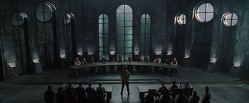 Movie still from “The Matrix Revolutions” (2003), directed by Lilly Wachowski – A man standing in front of a group of people in front of a large table; Wide shot, High angle