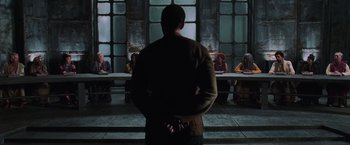 Movie still from “The Matrix Revolutions” (2003), directed by Lilly Wachowski – A man standing in front of a group of people in a room; Wide shot, Over the shoulder angle