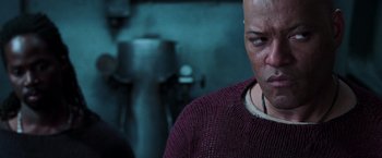 Movie still from “The Matrix Revolutions” (2003), directed by Lilly Wachowski – A bald man in a purple sweater looking at a camera; Close Up shot, Over the shoulder angle