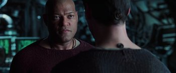 Movie still from “The Matrix Revolutions” (2003), directed by Lilly Wachowski – A man with a bald head is looking at another man in a dark room; Close Up shot, Over the shoulder angle
