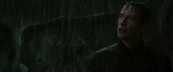 Movie still from “The Matrix Revolutions” (2003), directed by Lilly Wachowski – A man standing in the rain looking at the camera; Close Up shot, Low angle