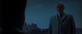 Movie still from “The Matrix Revolutions” (2003), directed by Lilly Wachowski – An older man standing in front of a city skyline at night; Medium shot, Over the shoulder angle