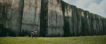 Movie still from “The Maze Runner” (2014), directed by Wes Ball – Two people walking in front of a tall concrete wall; Extreme Wide shot, Low angle
