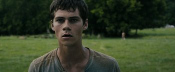 Movie still from “The Maze Runner” (2014), directed by Wes Ball – A young man standing in a field with trees in the background; Close Up shot, Low angle
