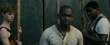 Movie still from “The Maze Runner” (2014), directed by Wes Ball – A man in a tan shirt is standing in front of a wall; Close Up shot, Low angle