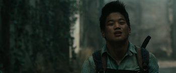 Movie still from “The Maze Runner” (2014), directed by Wes Ball – A young man in a green shirt is standing in the woods; Close Up shot, Low angle