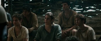 Movie still from “The Maze Runner” (2014), directed by Wes Ball – A group of men sitting next to each other in a cave; Medium shot, Over the shoulder angle