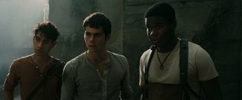 Movie still from “The Maze Runner” (2014), directed by Wes Ball – Two young men standing next to each other in front of a stone wall; Medium shot, Low angle