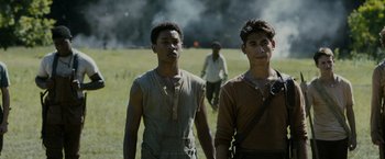 Movie still from “The Maze Runner” (2014), directed by Wes Ball – Two young men walking in a field with smoke in the background; Medium shot, Low angle
