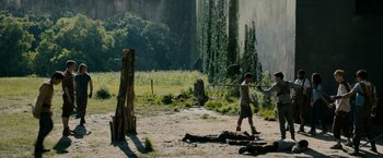 Movie still from “The Maze Runner” (2014), directed by Wes Ball – A man walking across a dirt field next to trees; Extreme Wide shot, High angle