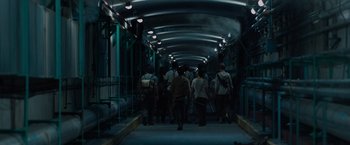 Movie still from “The Maze Runner” (2014), directed by Wes Ball – A group of people walking down a dark hallway; Wide shot, High angle