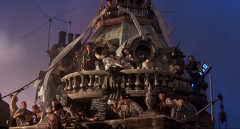 Movie still from “The Meaning of Life” (1983), directed by Terry Jones – A group of people sitting on top of a building; Wide shot, Low angle