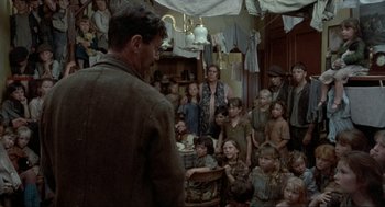 Movie still from “The Meaning of Life” (1983), directed by Terry Jones – A group of people gathered in a room; Wide shot, Over the shoulder angle