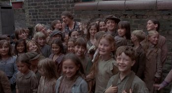 Movie still from “The Meaning of Life” (1983), directed by Terry Jones – A large group of children standing next to each other in front of a brick wall; Medium shot, High angle