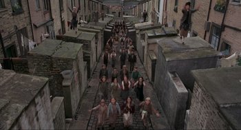 Movie still from “The Meaning of Life” (1983), directed by Terry Jones – A group of people standing on a brick walkway; Extreme Wide shot, High angle