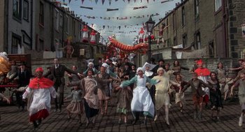 Movie still from “The Meaning of Life” (1983), directed by Terry Jones – A group of people in costumes on a brick street; Extreme Wide shot, High angle