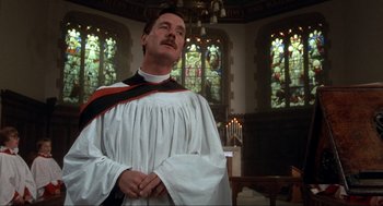 Movie still from “The Meaning of Life” (1983), directed by Terry Jones – A man in a priest's outfit stands in a church; Medium shot, Low angle
