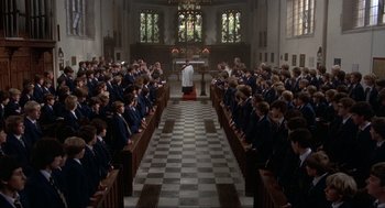 Movie still from “The Meaning of Life” (1983), directed by Terry Jones – A group of people sitting in rows in front of a priest; Extreme Wide shot, High angle