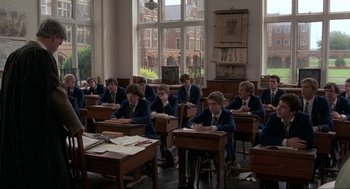 Movie still from “The Meaning of Life” (1983), directed by Terry Jones – A group of young men sitting at desks in front of a large window; Wide shot, High angle