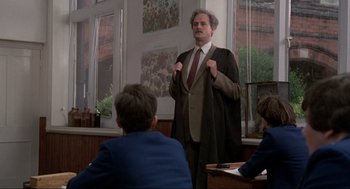 Movie still from “The Meaning of Life” (1983), directed by Terry Jones – A man standing in front of a group of people; Medium shot, Low angle